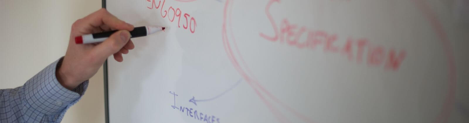 A hand gripping a red board marker to write on a whiteboard to help illustrate GB Electronics' compliance services.
